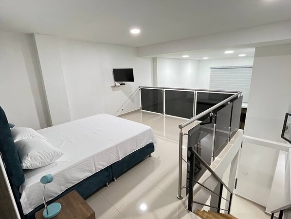 A modern bedroom with a bed, a desk, a TV, and a balcony with a glass railing.