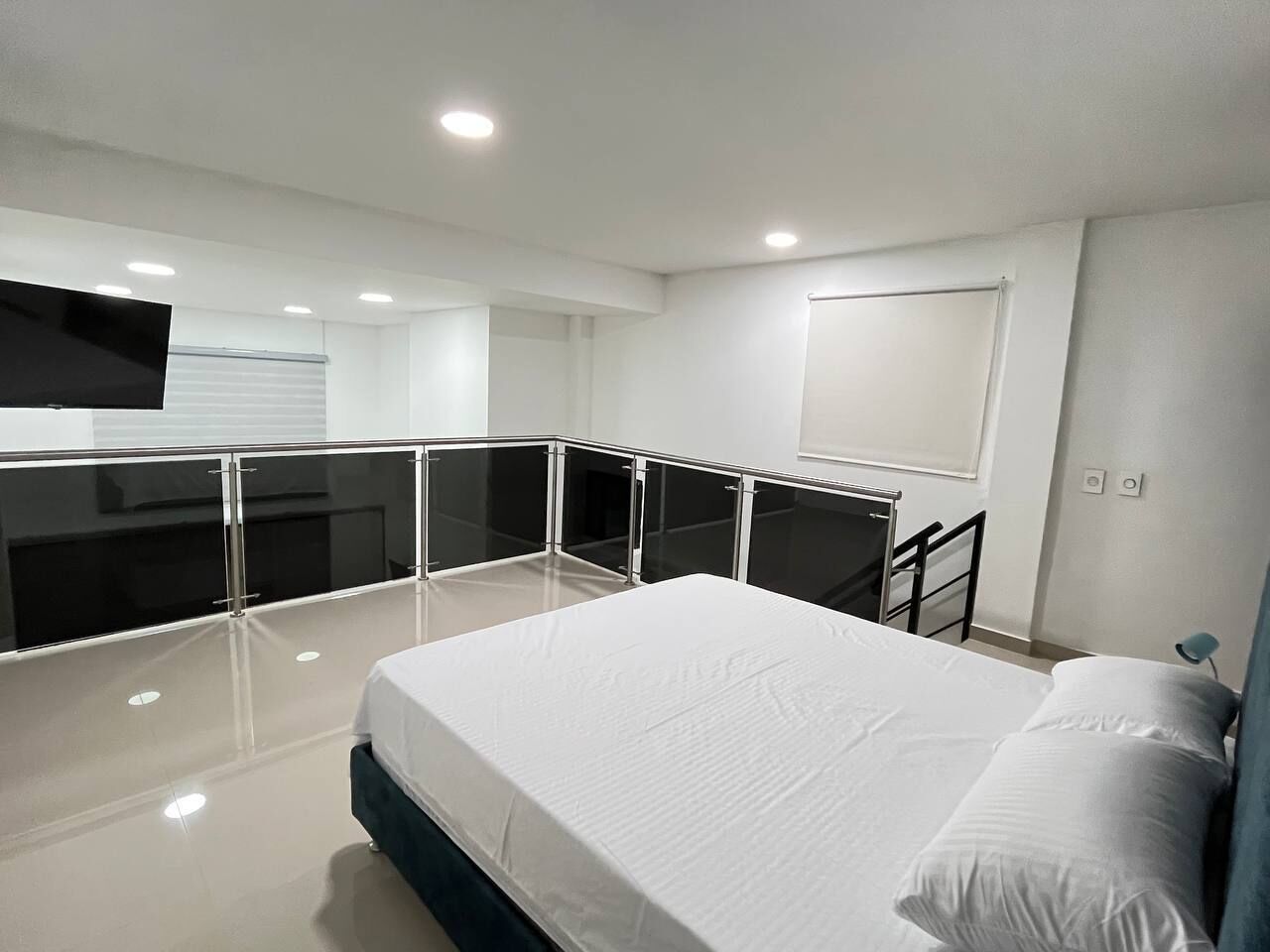 Un dormitorio moderno con una cama grande, un balcón con cerramiento de vidrio y un televisor de pantalla plana montado en la pared.