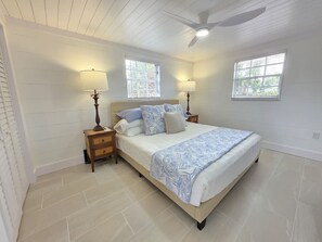 A bedroom with a bed, two nightstands, a ceiling fan, and two windows.