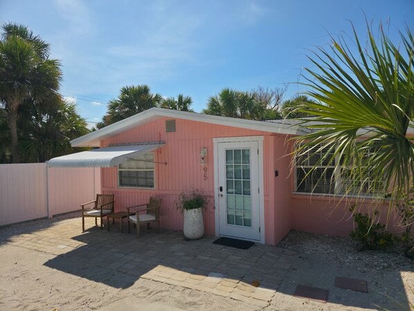 Una casa móvil rosa con un porche cubierto, una puerta y un pequeño jardín.