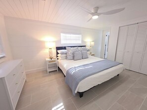 A bedroom with a bed, nightstands, a dresser, a ceiling fan, and a window with blinds.