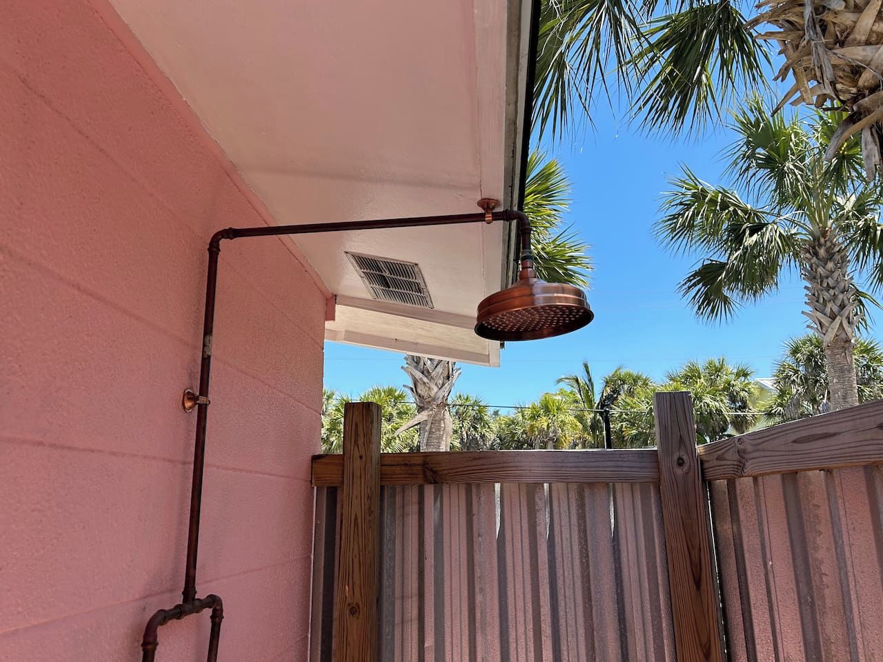 Un luminaire extérieur en métal, fixé au mur extérieur d’un bâtiment, avec une clôture en bois en arrière-plan.