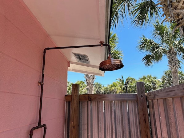 A metal outdoor light fixture attached to a building's exterior wall, with a wooden fence in the background.