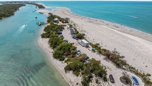 Vue aérienne d’une zone côtière comprenant une plage, un port de plaisance et un parking.