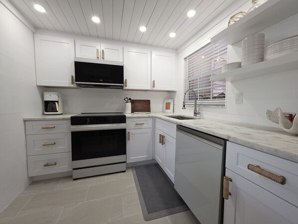 A modern kitchen with white cabinetry, a built-in oven, a microwave, and a sink.