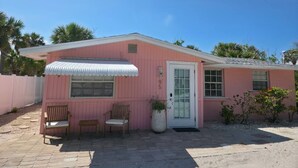 Un bâtiment rose, de plain-pied, avec une porte blanche, deux fenêtres et un petit porche agrémenté de deux chaises en bois.