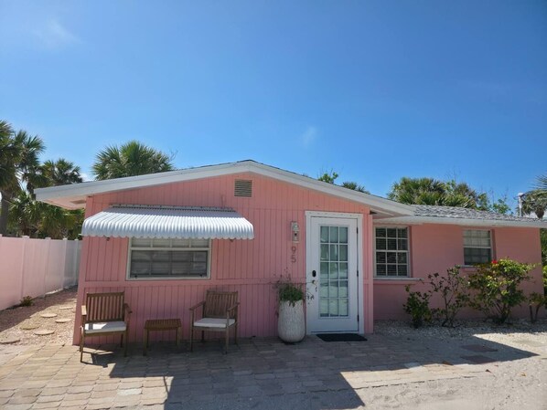 A pink building with a white door, two wooden benches, and a potted plant.