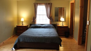 Une chambre à coucher avec un grand lit, deux tables de chevet avec des lampes, une fenêtre avec des rideaux, un miroir et un plancher en bois.