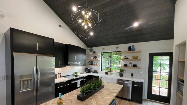 Une cuisine moderne dotée d’un îlot central, de meubles de rangement noirs, d’appareils électroménagers en acier inoxydable et d’un plan de travail au motif en chevrons.