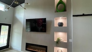 Un salon moderne avec une cheminée, un téléviseur fixé au mur et des étagères décoratives.
