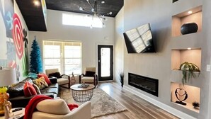 Een ruime woonkamer met een moderne haard, een grote televisie aan de muur en een gezellige zithoek met een bank en fauteuils.