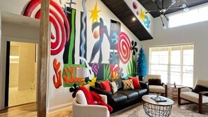 Een moderne woonkamer met een kleurrijke abstracte muurschildering, een leren zwarte bank, witte fauteuils en een ronde salontafel.