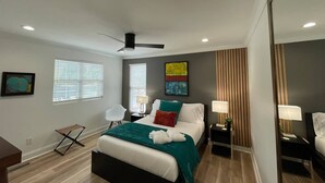 Een moderne slaapkamer met een bed, nachtkastjes, een stoel en een plafondventilator.