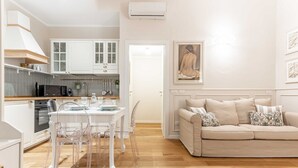 A modern kitchen with white cabinets, a dining table with chairs, and a beige sofa in a living area. - Hostmate - Milano - Ticinese (Milano)