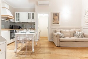 A modern kitchen with white cabinets, a dining table with chairs, and a beige sofa in a living area. - Hostmate - Milano - Ticinese (Milano)