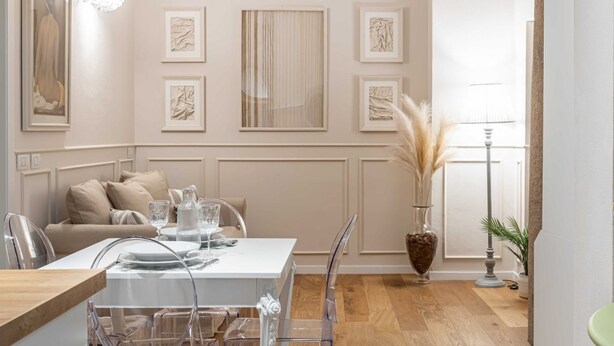 A dining area with a white table set for four, clear chairs, a sofa with beige cushions, and artwork on the walls. - Hostmate - Milano - Ticinese (Milano)