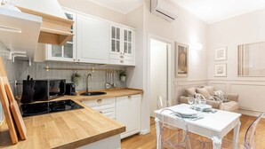 A modern kitchen with white cabinets, a wooden countertop, and a dining area with a white table and chairs. - Hostmate - Milano - Ticinese (Milano)