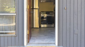 A doorway leading to a kitchen with stainless steel appliances, a doormat with "hello" written on it, and a wall-mounted light fixture.
