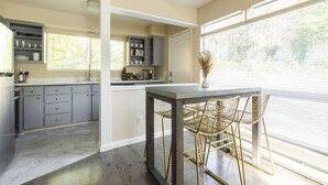A modern kitchen with grey cabinets, a marble countertop, and a dining area with a table and chairs.