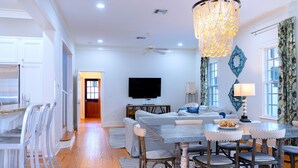 A modern living room with a dining area, a flat-screen TV, and a chandelier.