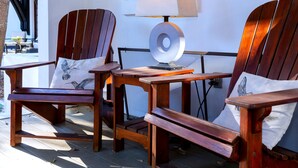 Two wooden Adirondack chairs with cushions, a small wooden table, and a floor lamp.