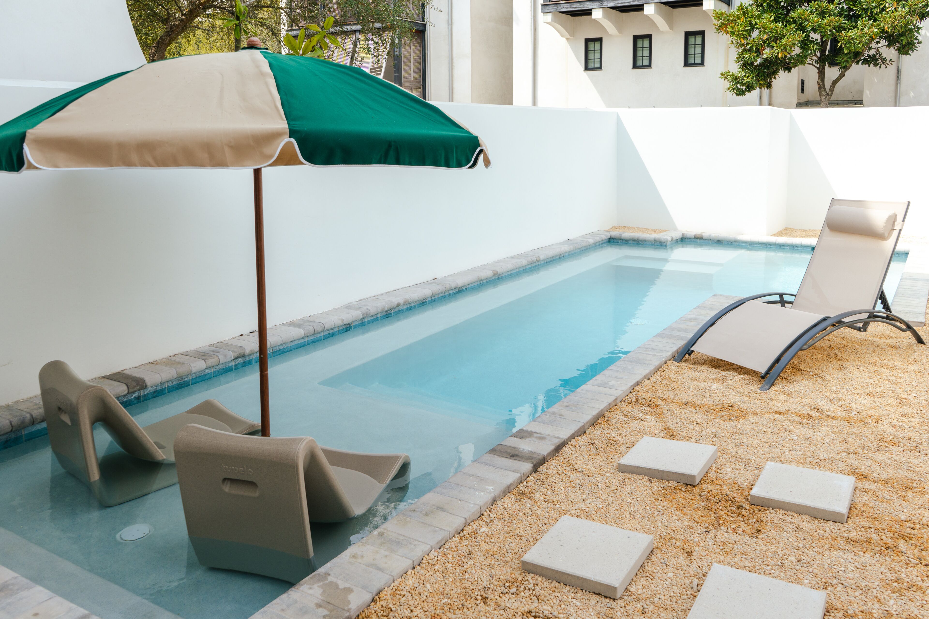 Un área de piscina con una tumbona y un paraguas verde.