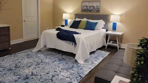 A bedroom with a bed, bedside lamps, a nightstand, a door, a framed picture on the wall, and a patterned rug. - Beautiful farm stay apartment, rural Georgetown KY (Georgetown)