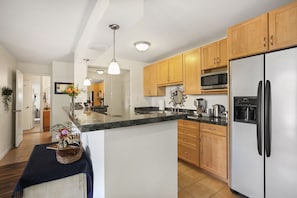 A modern kitchen with wooden cabinets, a stainless steel refrigerator, a microwave, and a granite countertop.