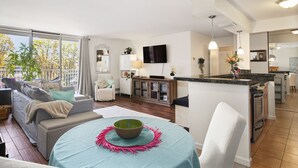 Uma sala de estar moderna com um sofá, uma mesa de jantar com uma tigela, e uma área de cozinha com uma televisão.