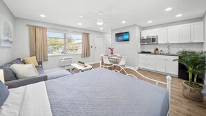 A modern bedroom with a large bed, a small dining table, and a kitchenette. - Bayview Regency Apartments By Lowkl (Fort Lauderdale)