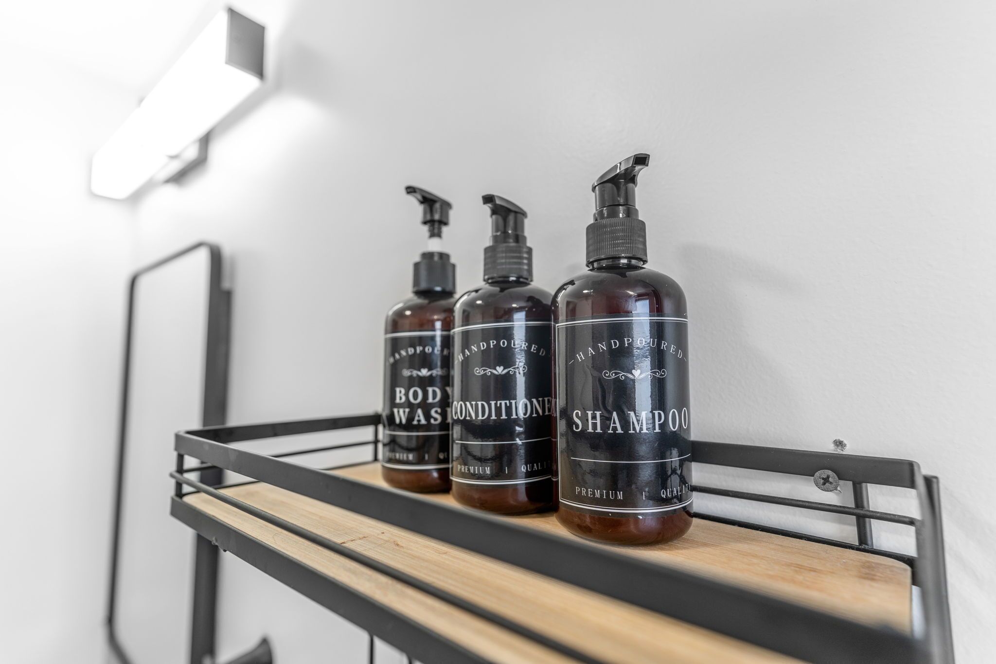 Drei Flaschen handgegossenes Duschgel und Shampoo auf einem Metallregal vor einer weißen Wand.