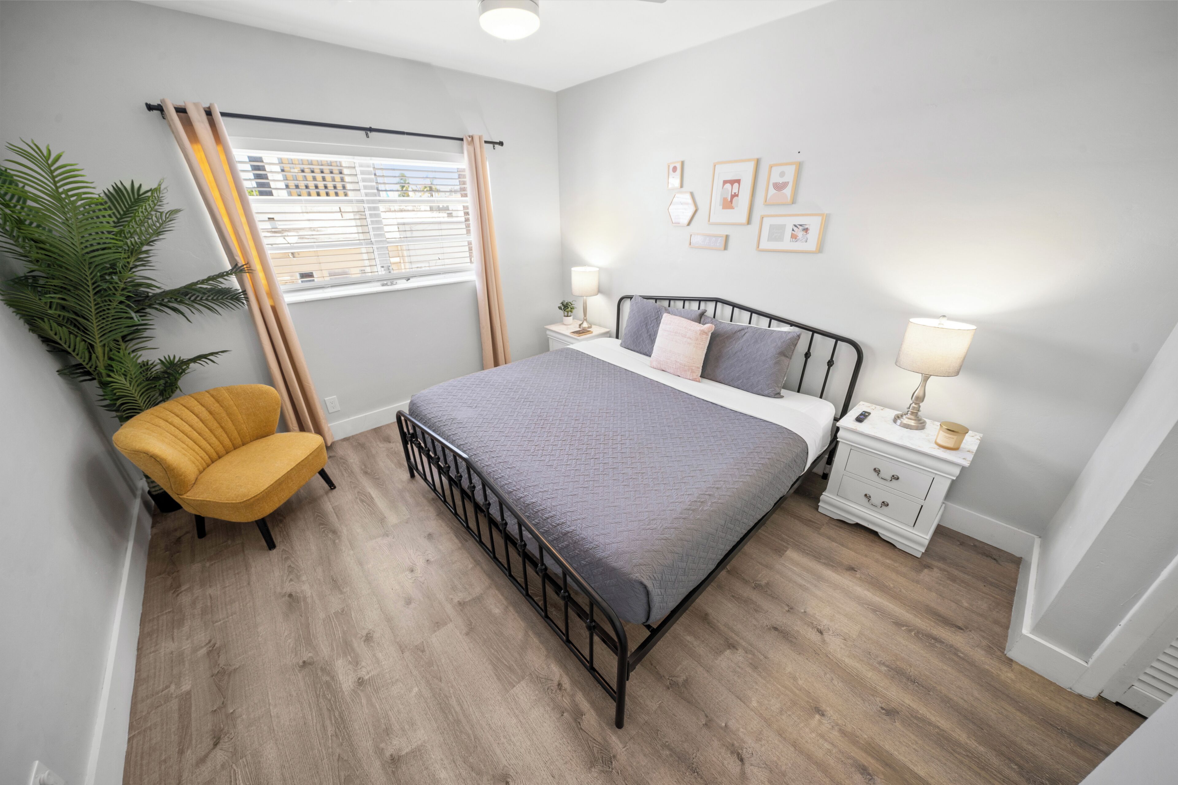 A bedroom with a bed, a nightstand, a lamp, a chair, a window with curtains, and a plant.