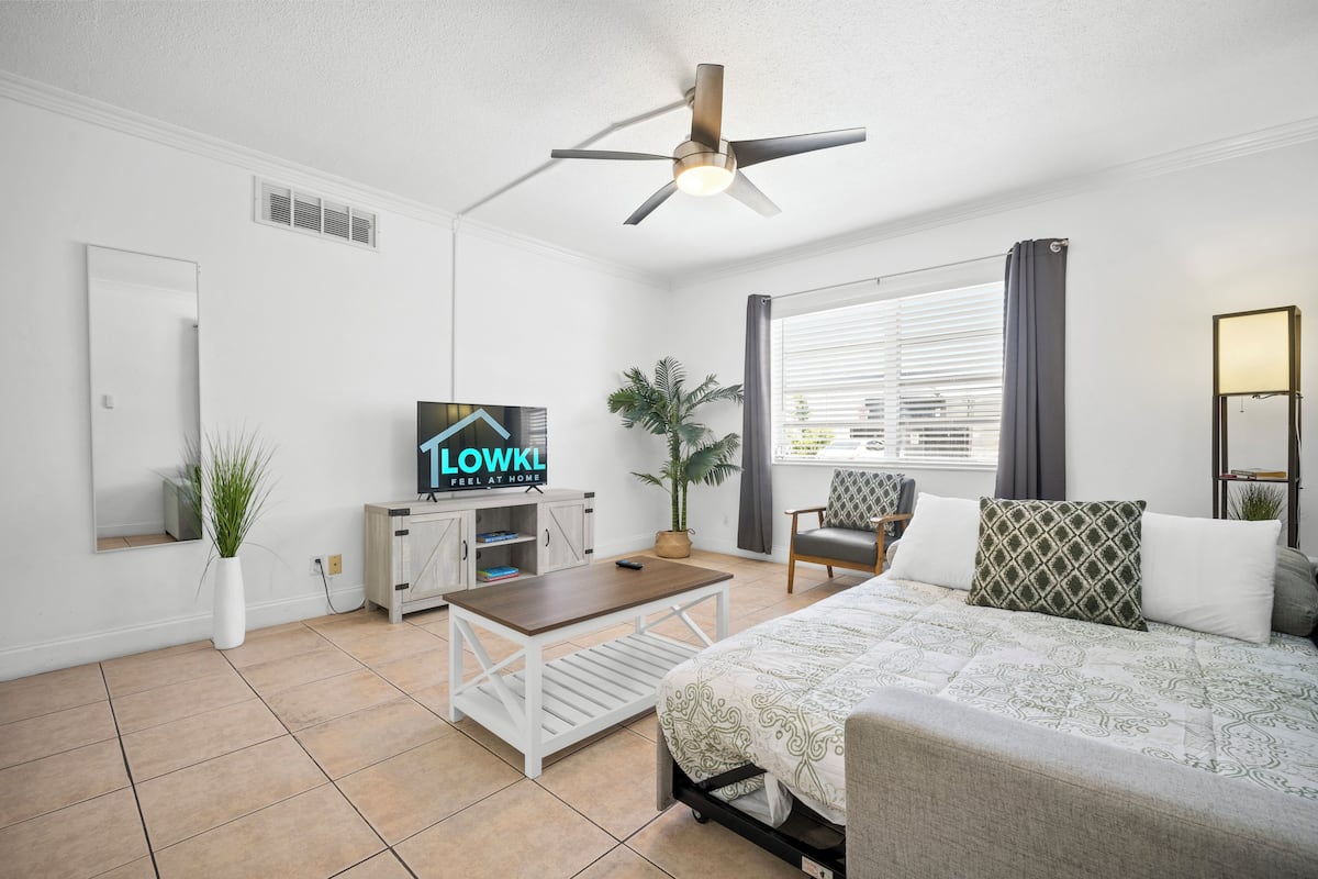 A modern hotel room with a bed, a desk, a television, and a ceiling fan.