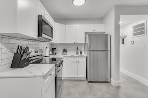 A modern kitchen with white cabinets, stainless steel appliances, and a marble countertop. - Bayview Regency Apartments By Lowkl (Fort Lauderdale)