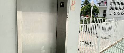 Una entrada cerrada con un portón metálico, un letrero de seguridad contra incendios y una escalera que conduce a un edificio con balcones.
