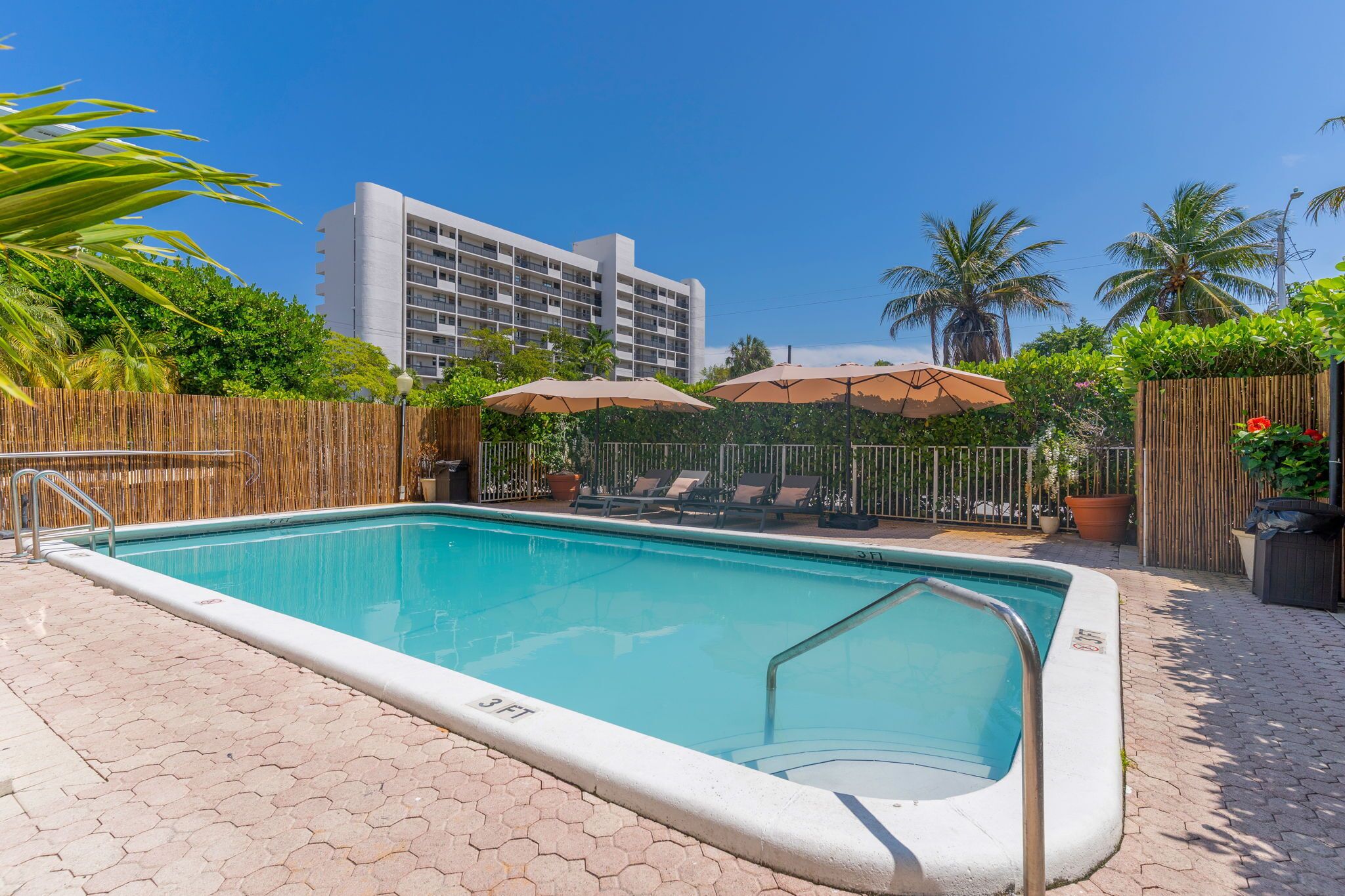 A swimming pool with a wooden fence, lounge chairs, and umbrellas.