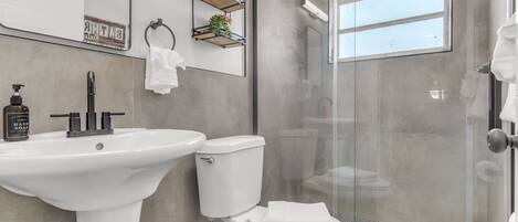 Un baño moderno con lavamanos pedestal, inodoro y ducha con mampara de vidrio.