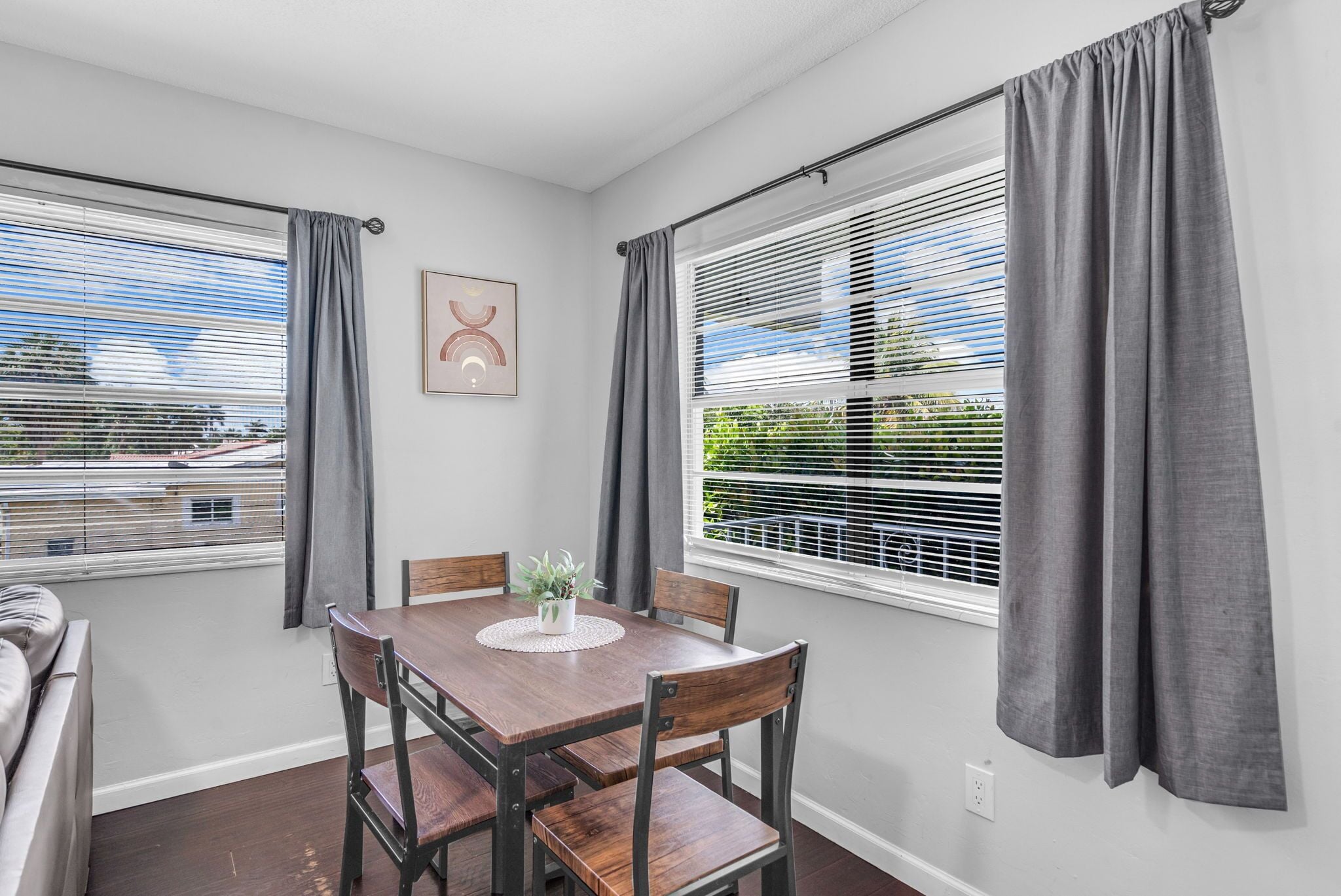 A dining area with a wooden table and chairs, a potted plant, and a view through window blinds.