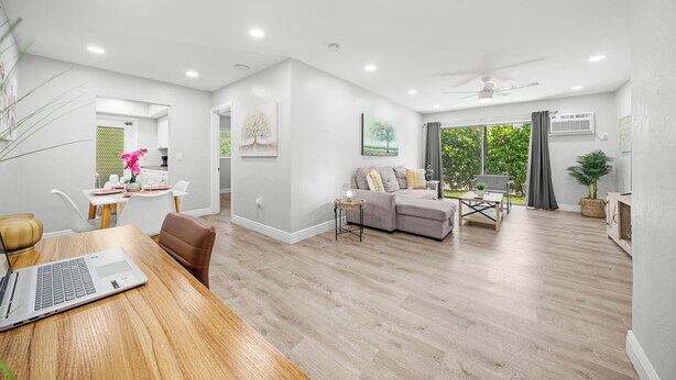 A modern living room with a dining area, a sofa, and a laptop on a wooden table. - Bayview Regency Apartments By Lowkl (Fort Lauderdale)