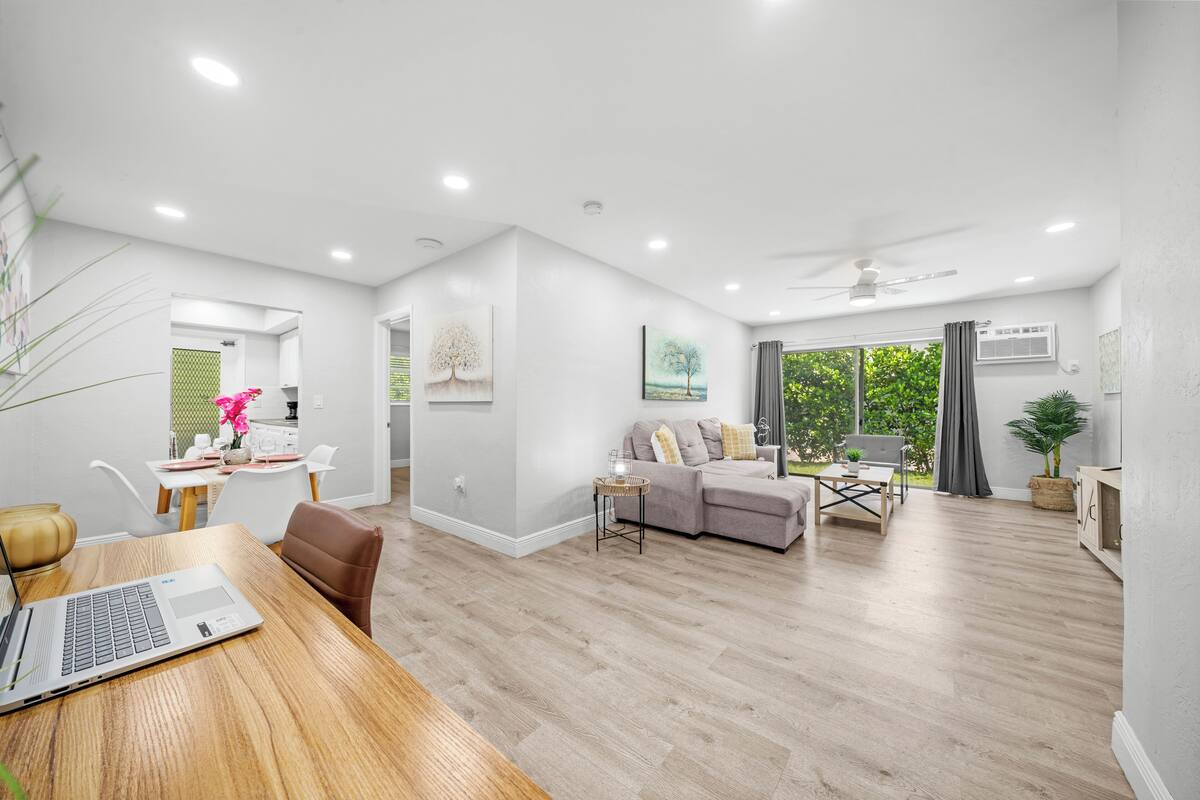 A modern living room with a dining area, a sofa, and a laptop on a wooden table.