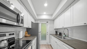 A modern kitchen with white cabinets, stainless steel appliances, and a grey countertop. - Bayview Regency Apartments By Lowkl (Fort Lauderdale)