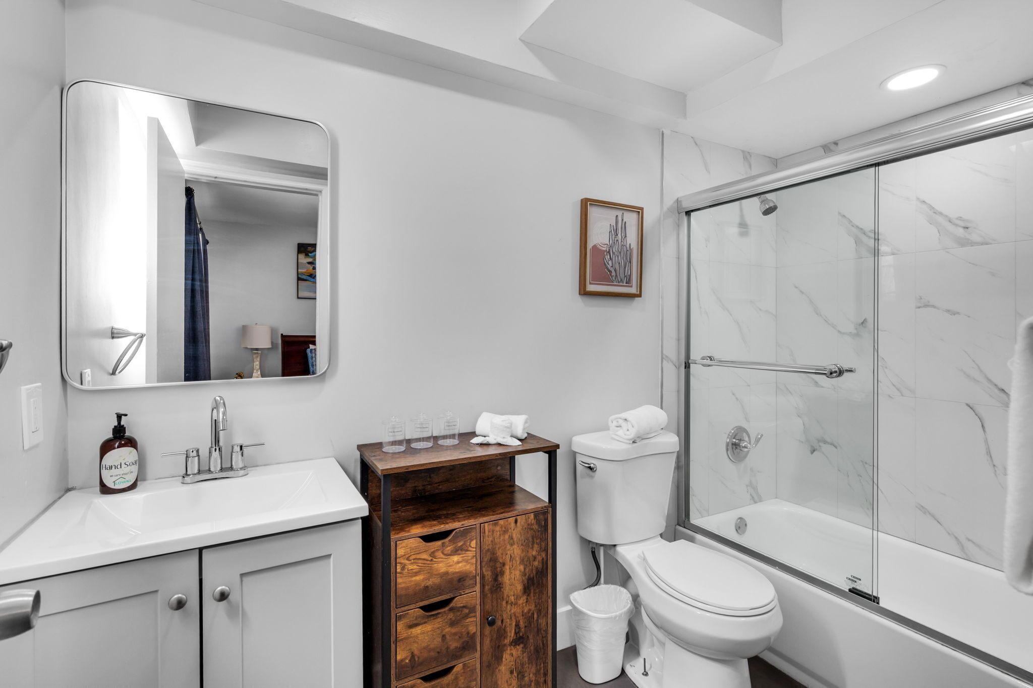 Een moderne badkamer met een witte wastafel, een houten kastje, een toilet en een douche met glazen wanden.