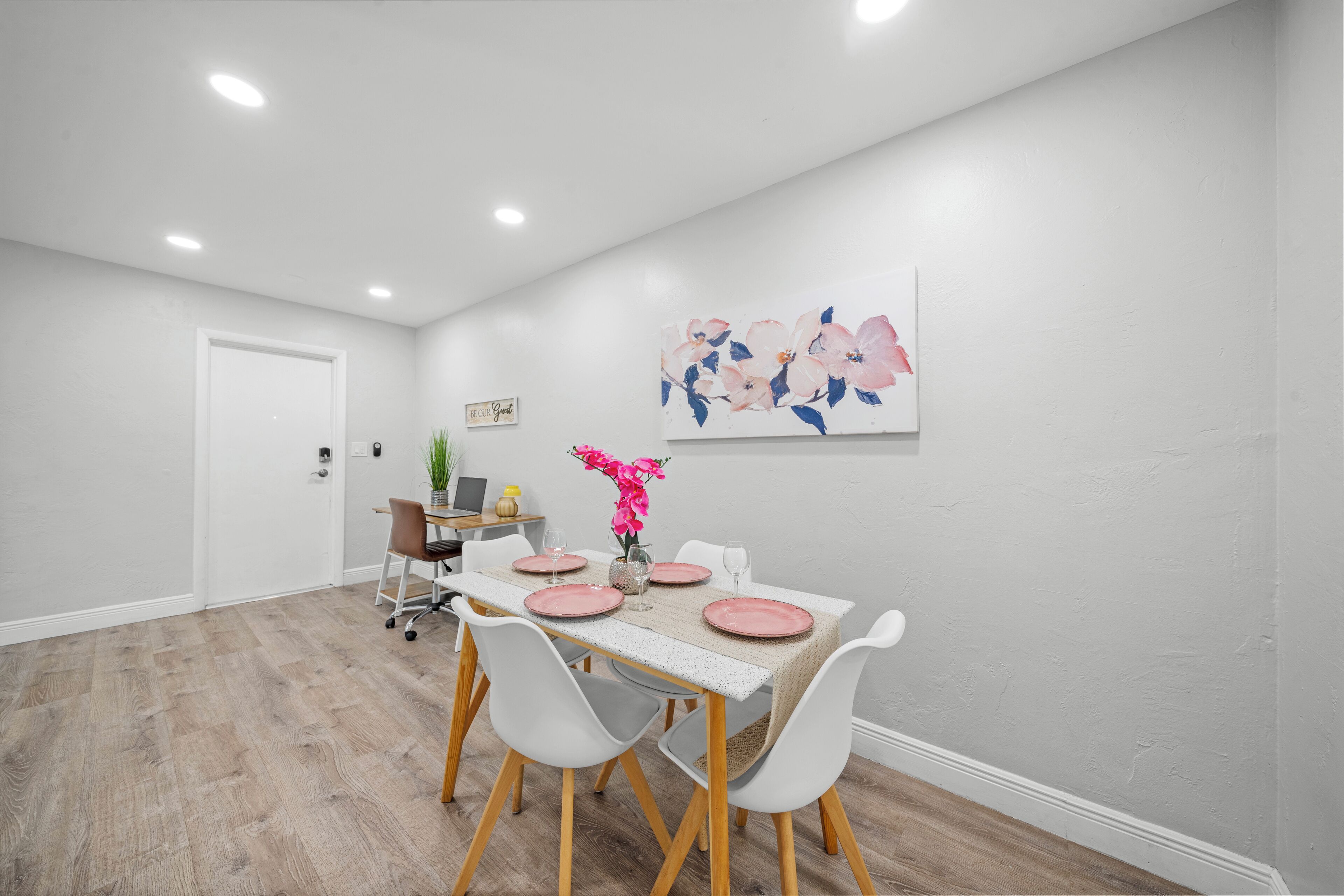 A dining area with a table set for four, white chairs, and a decorative wall piece.