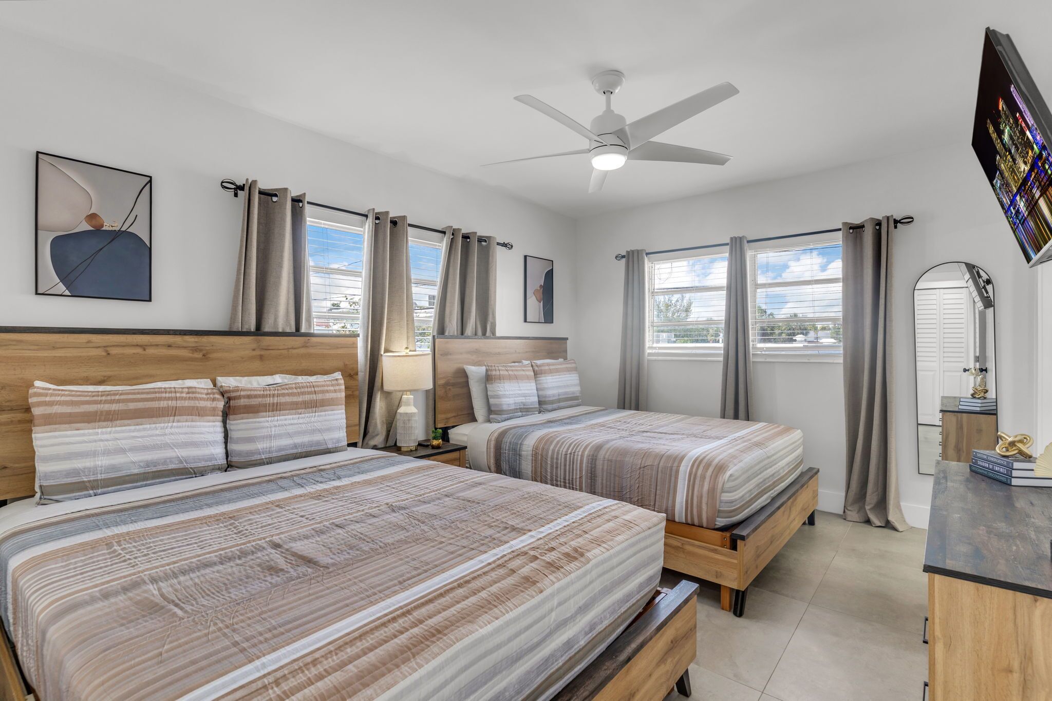 A hotel room with two beds, a ceiling fan, a large window, and a TV mounted on the wall.