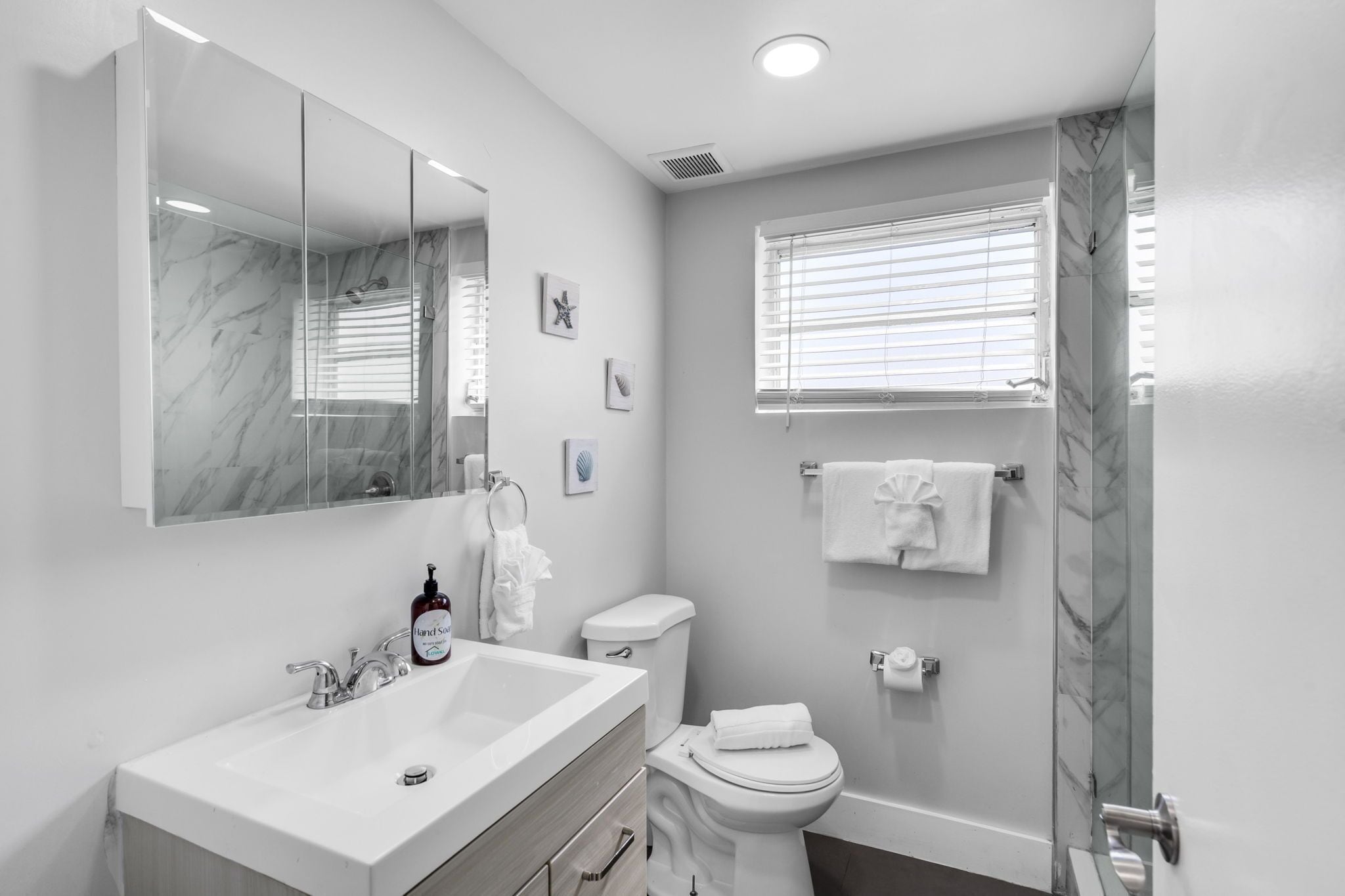 Une salle de bain moderne avec un lavabo en marbre, des toilettes et une douche dotée d’une porte en verre.