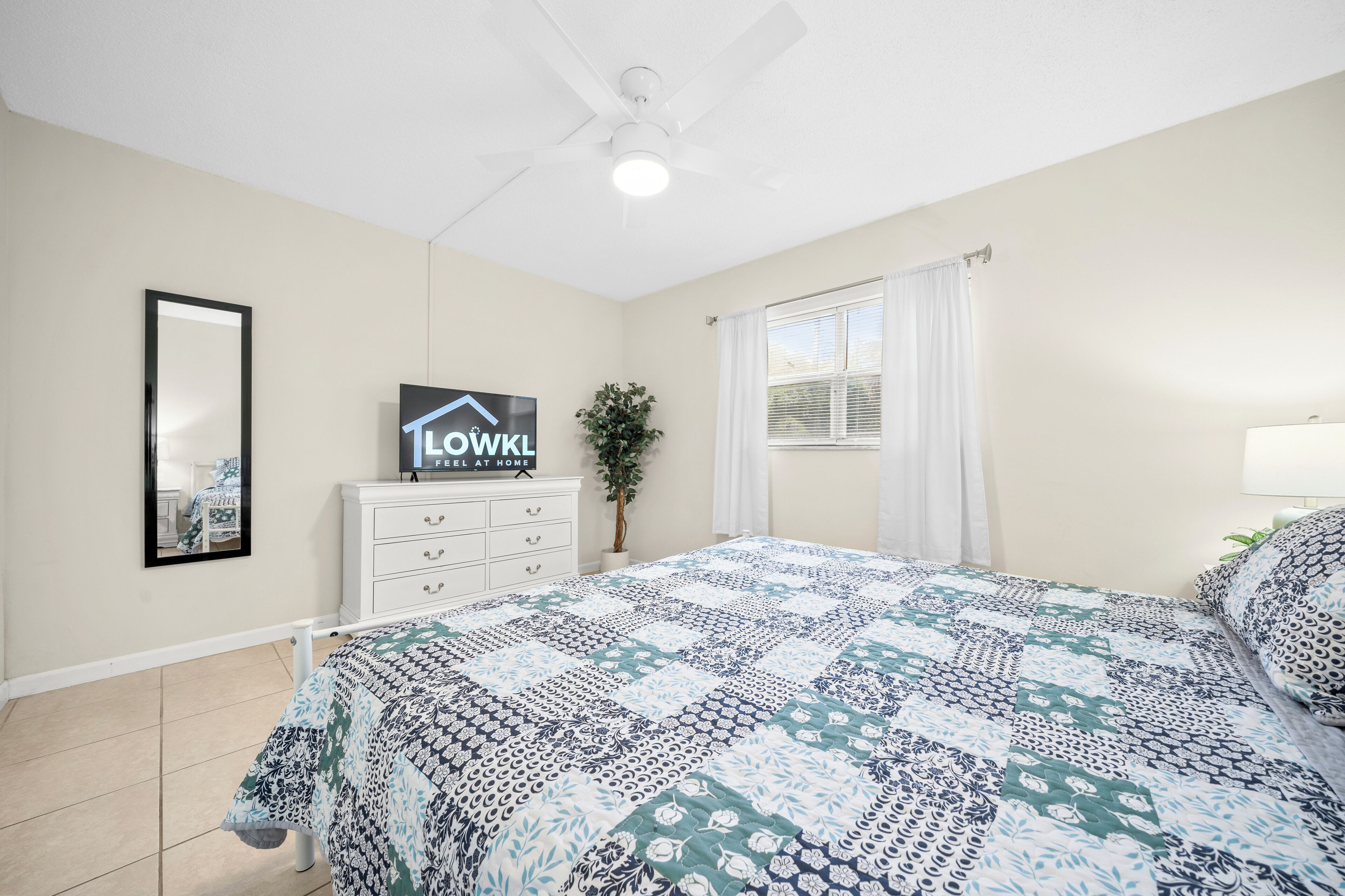 Une chambre à coucher avec un lit, un ventilateur de plafond, une commode, un miroir et un panneau accroché au mur.