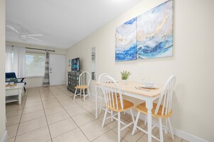 A dining area with a table and chairs, a ceiling fan, a TV, and a painting on the wall.
