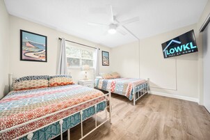 Un dormitorio con dos camas, ventilador de techo y televisor mostrando 'LOWKL FEEL AT HOME'.