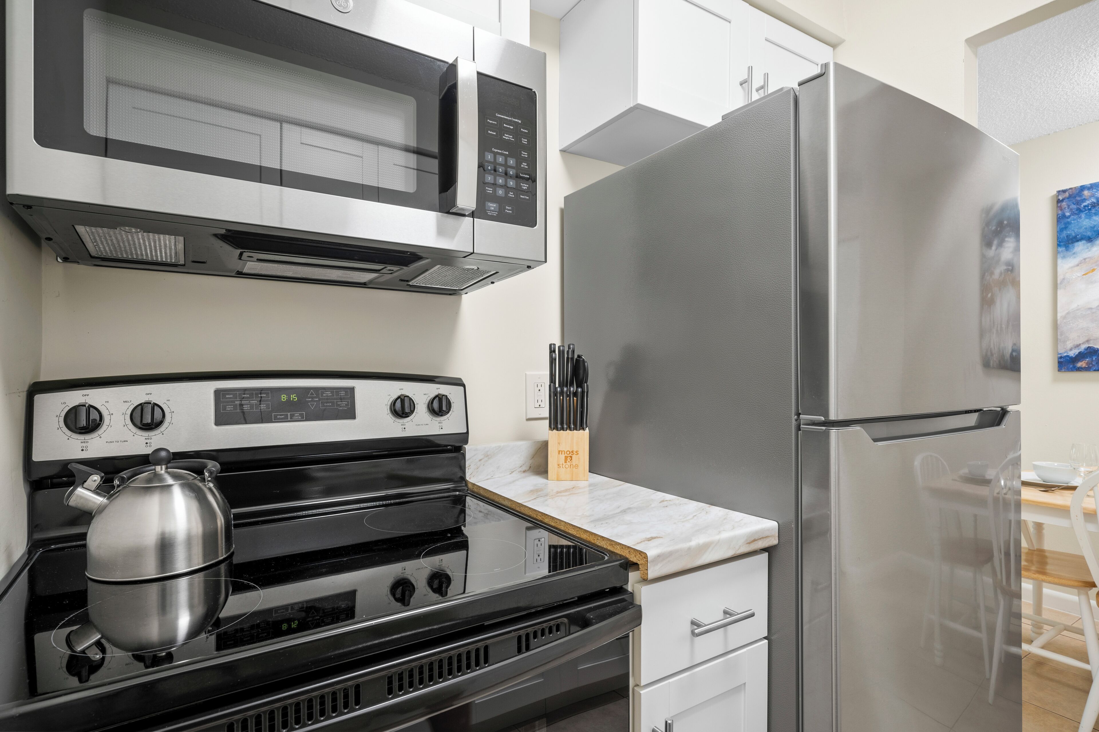 A kitchen with a stainless steel refrigerator, a microwave, an oven, and a kettle.