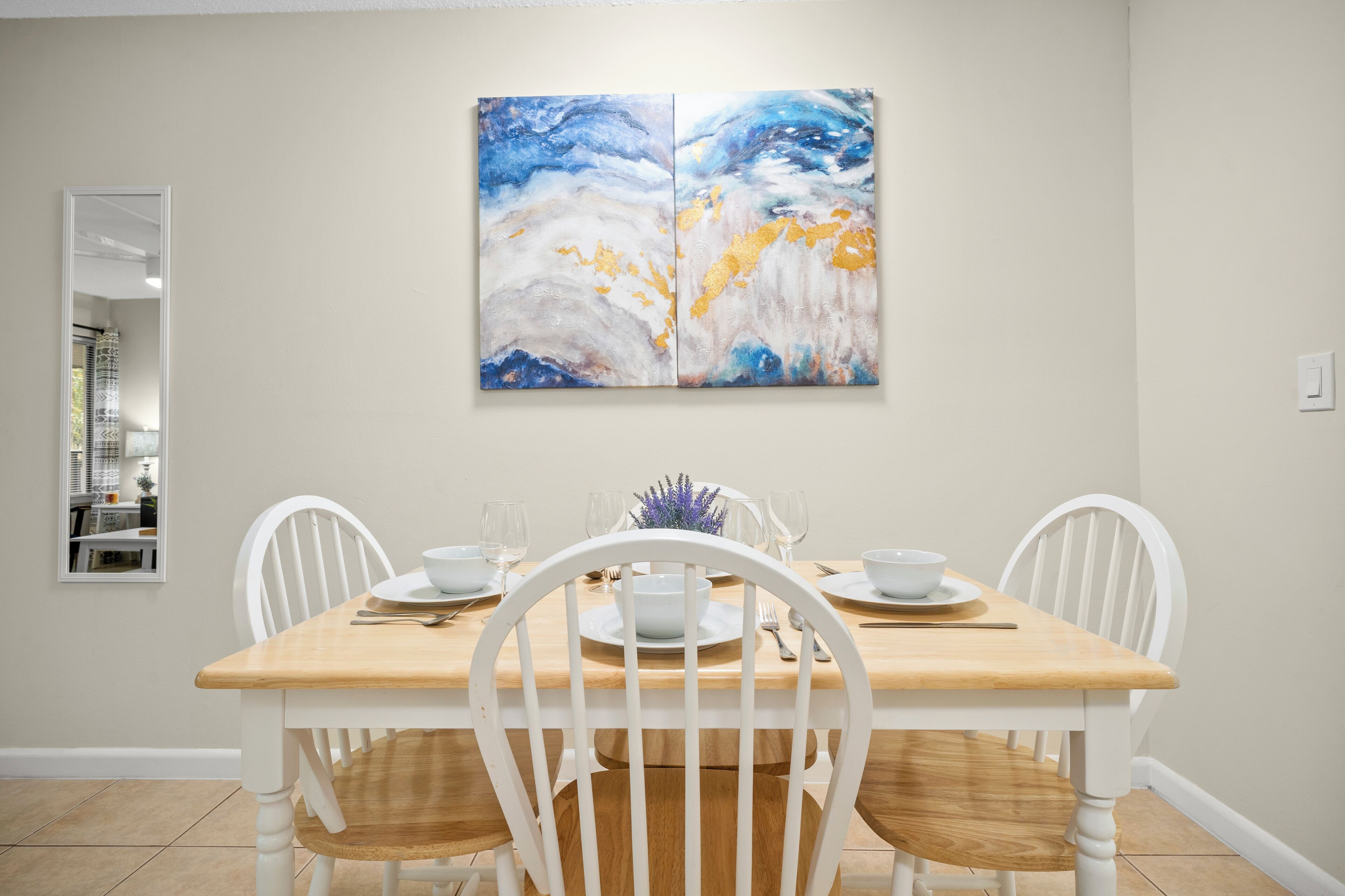 Un coin repas avec une table en bois, des chaises blanches et un grand tableau abstrait accroché au mur.